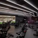 A dimly lit gym featuring a dark gray, textured rubber floor. Several indoor cycling bikes are arranged on the floor. Sources and related content.