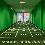 A gym with a green artificial turf track marked with numbered squares on a dark floor.
