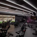 A dimly lit gym featuring a dark gray, textured rubber floor. Several indoor cycling bikes are arranged on the floor. Sources and related content.