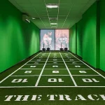 A gym with a green artificial turf track marked with numbered squares on a dark floor.