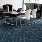 An executive office space featuring a dark blue carpet with a subtle geometric grid pattern, a large wooden desk, and white visitor chairs.