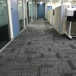 Office hallway with patterned grey carpet and glass-walled offices.