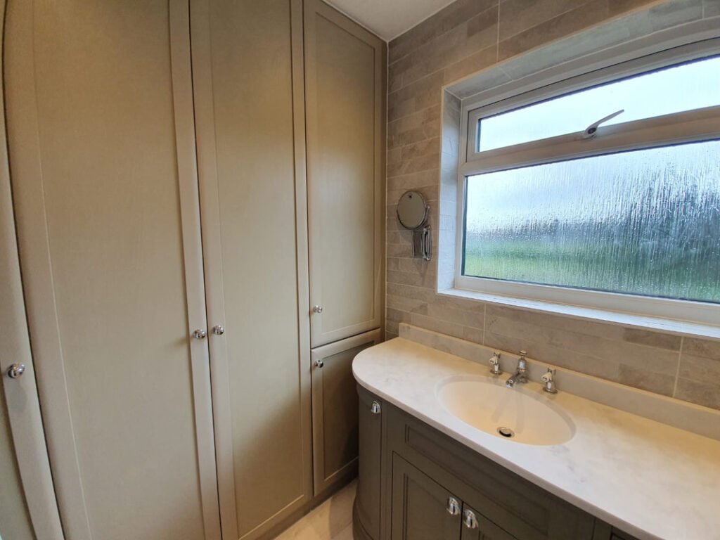 bathroom-vanity-installation-with-curved-grey-painted-vanity-unit-marble-worktop-chrome-taps-and-tall-fitted-storage-cupboards-with-chrome-knobs