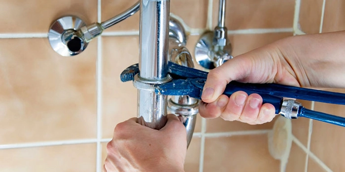 plumber-using-a-wrench-to-repair-bathroom-basin-pipework-and-chrome-fittings-against-a-tiled-wall